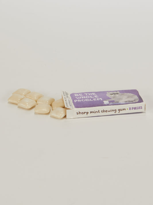 A pack of Blue Q’s Be The Whole Problem Gum, mint-flavored with 8 pieces—some peeking out of the box. The box features the phrase "BE THE WHOLE PROBLEM" and a small animal illustration.