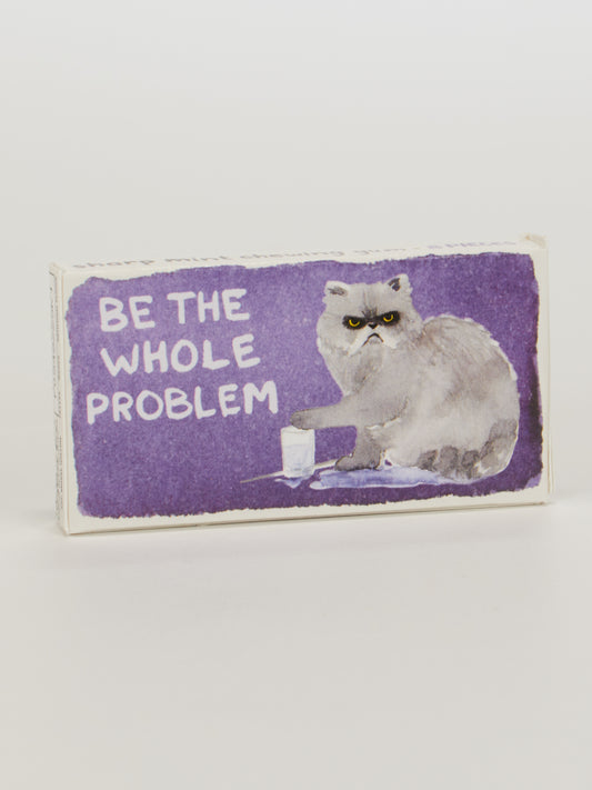 The Blue Q "Be The Whole Problem Gum" features a box with a grumpy gray cat knocking over milk on a purple background and bold white text. Each box contains 8 pieces of candy-coated gum inside.