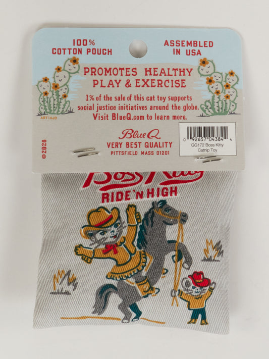 The Blue Q Boss Kitty Catnip Toy is a cotton pouch with organic catnip, showing a cartoon cowboy cat on horseback. Packaging highlights healthy play and notes that 1% of sales goes to social initiatives.