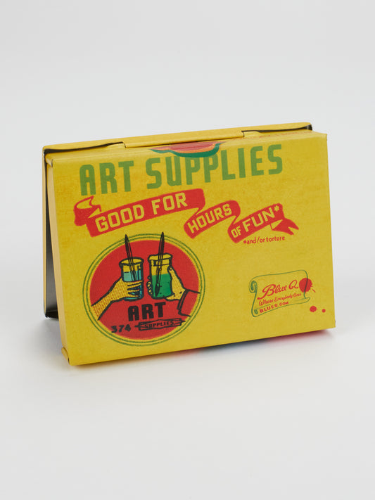 A yellow tin labeled “Art Supplies” with retro-style graphics—featuring paintbrushes in jars and the playful phrase “Good for hours of fun* and/or torture.” This compact storage box is the Art Supplies Pocket Box from Blue Q, with the brand name printed in the lower right corner.