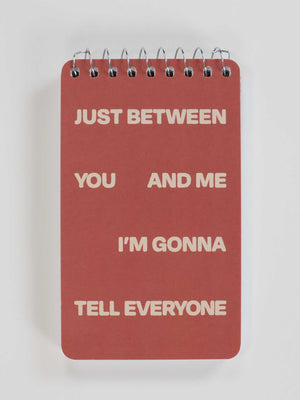 The Blue Q Just Between You And Me I'm Gonna Tell Everyone 3x5 Spiral Notebook features a bold red cover with beige text, playfully highlighting how tough it is to keep a secret.