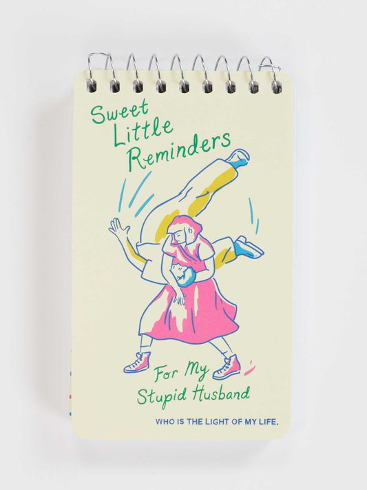 Blue Q’s "Sweet Little Reminders For My Stupid Husband" 3x5 spiral notebook features a playful cover illustration—an ideal romantic gift with the message: Sweet Little Reminders For My Stupid Husband. WHO IS THE LIGHT OF MY LIFE.