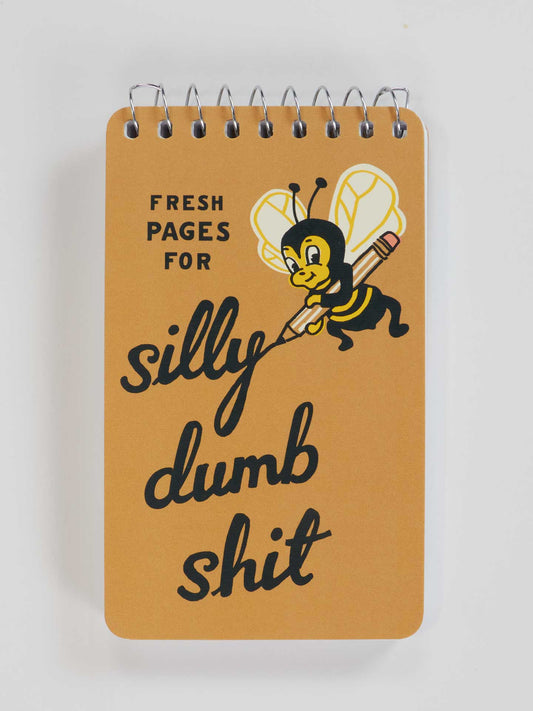 The Blue Q Silly Dumb Shit 3x5 Spiral Notebook features a yellow cover with a bee holding a pencil and the playful phrase: "Fresh pages for silly dumb shit" in black lettering.