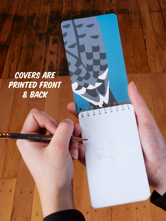 A person holds the Blue Q “I’m Really Into Birds. Take-Along Notebook”—a compact 3x5 spiral notebook featuring bird designs on both the front and back covers. The notebook is open to reveal sketches on the first page, making it ideal for jotting down observations. Text reads: COVERS ARE PRINTED FRONT & BACK.