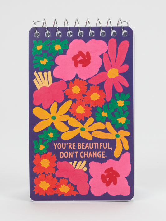 Introducing the Blue Q “You’re Beautiful Don’t Change” 3x5 Spiral Notebook: a purple notebook featuring cheerful flower illustrations and the uplifting message “YOURE BEAUTIFUL, DONT CHANGE.” printed at its center—perfect for anyone who needs a daily reminder to embrace themselves just as they are.