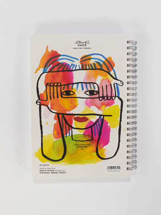 A 6" x 8" spiral-bound Blue Q notebook titled "Everything I'm Avoiding (Alphabetized)" features a vibrant abstract face and hands cover, with orange, yellow, pink, and blue splashes. Perfect for colorful organization.