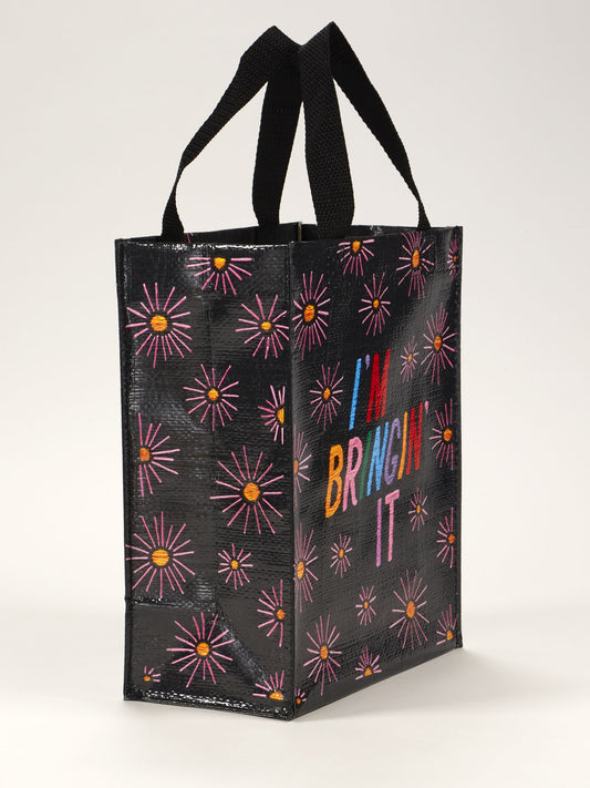 The Blue Q I'm Bringin' It Handy Tote is a reusable black bag with pink and orange starbursts, colorful "IM BRINGIN IT" text, and two sturdy black handles—perfect for carrying your essentials in bold style.
