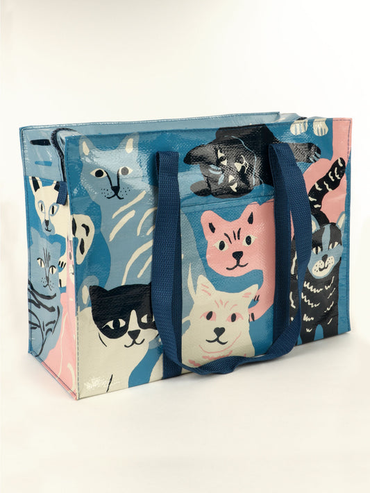 The Blue Q Happy Cats Shoulder Tote is a reusable bag featuring illustrated cats in blue, pink, cream, and black. It has thick blue handles, a glossy finish, and is shown on a plain white background.