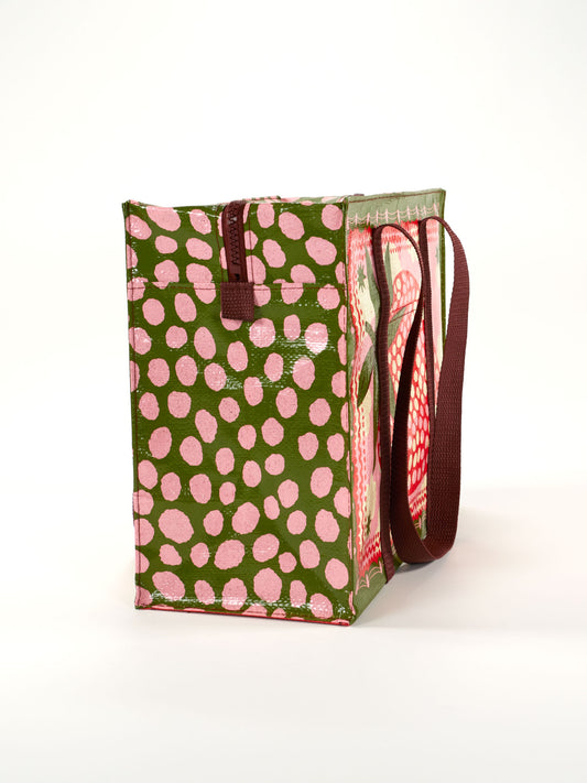 The Strawberry Clouds Shoulder Tote by Blue Q features an olive green background with pink polka dots, a side zipper, and a long brown strap, combining style and functionality.