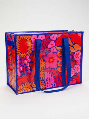 Introducing the Bright Blooms Shoulder Tote by Blue Q—a colorful, reusable bag featuring blue handles and vivid red, orange, and pink floral patterns set against a striking blue and red background. Made from eco-friendly recycled materials, this tote is both stylish and sustainable.