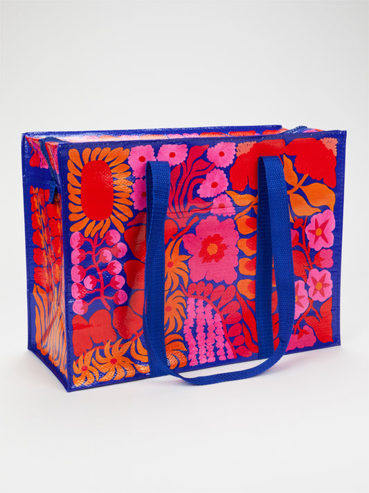 Introducing the Bright Blooms Shoulder Tote by Blue Q—a colorful, reusable bag featuring blue handles and vivid red, orange, and pink floral patterns set against a striking blue and red background. Made from eco-friendly recycled materials, this tote is both stylish and sustainable.