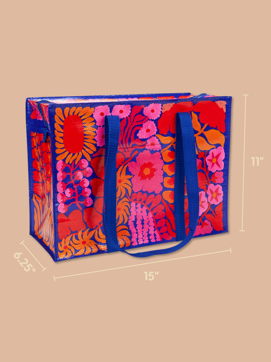 The Bright Blooms Shoulder Tote by Blue Q is a colorful floral bag made from eco-friendly, recycled material, featuring blue handles and borders. Displayed on a beige background, this vibrant tote measures 15 inches wide, 11 inches tall, and 6.25 inches deep.