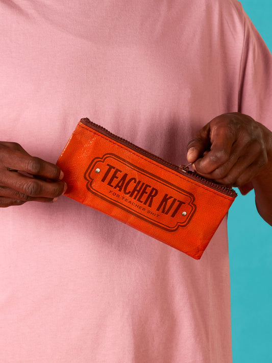 A person in a light pink shirt holds an orange Blue Q Teacher Kit Pencil Case against a blue background.