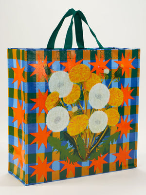 The Blue Q Dandelion Pop Shopper is a reusable bag with green handles, featuring yellow and white dandelions on a blue and green checkered background with orange stars.