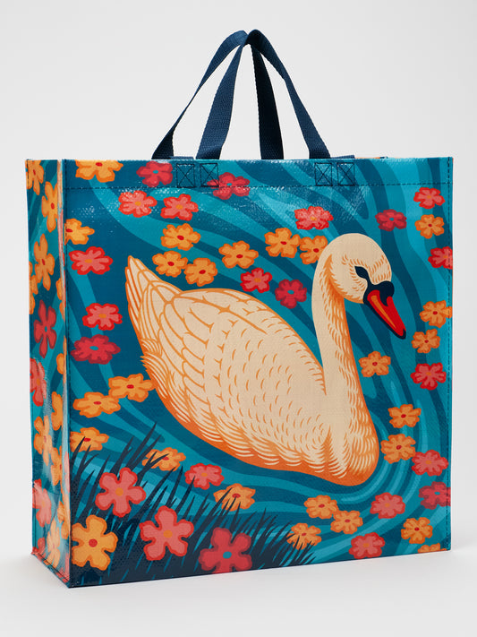 The Swan Shopper by Blue Q is a reusable, eco-friendly shopping bag with blue handles, featuring a swan amid orange, yellow, and pink flowers on a blue background with green grass accents.