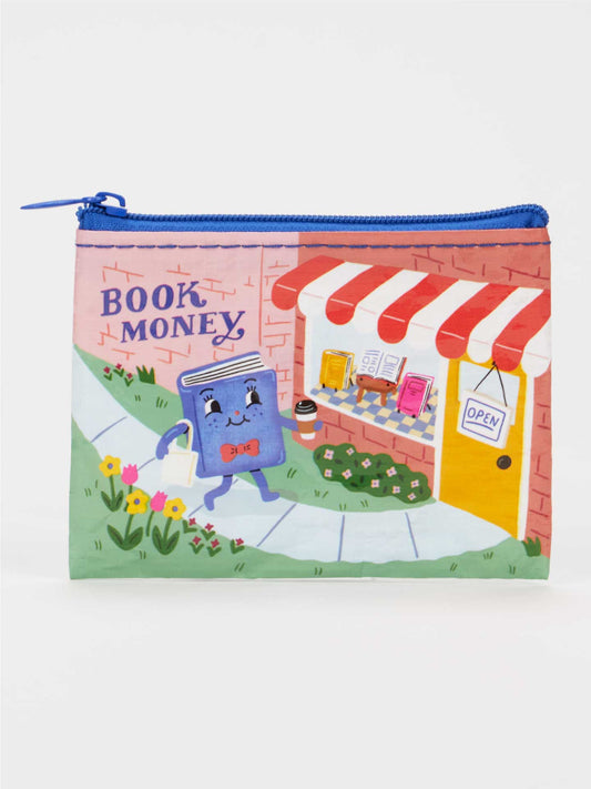 The Blue Q Book Money Coin Purse is a zippered pouch made from eco-friendly, recycled material, featuring an illustration of a smiling book character holding a coin and heading toward a charming shop with a red-striped awning, flowers, and a sign reading "BOOK MONEY"—a perfect accessory for any book lover.