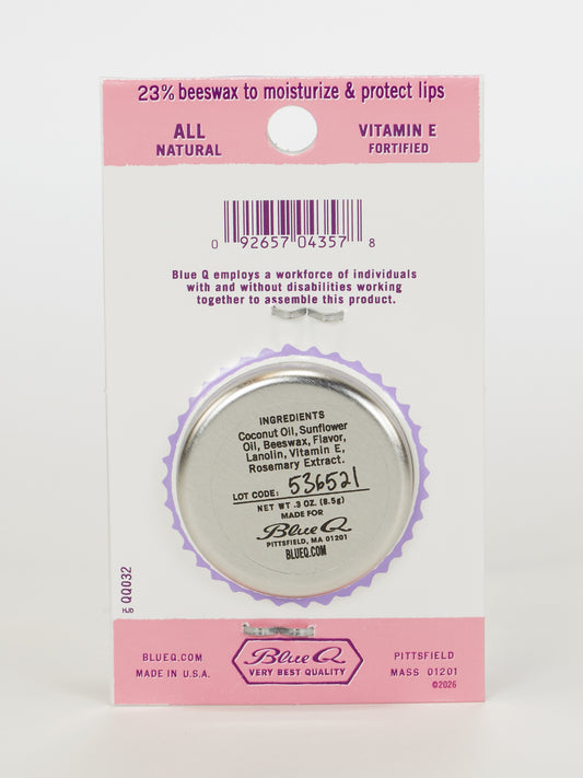A .3 oz tin of Blue Q Lip Shit Lip Balm–Everyone's Favorite Birthday Cake is attached to a card highlighting beeswax, vitamin E, an ingredient list, lot code, and employment of people with disabilities.