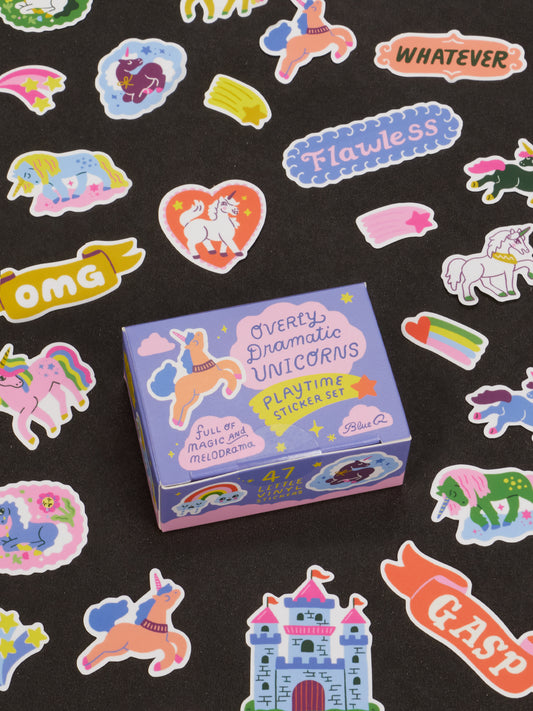 A box labeled Overly Dramatic Unicorns Playtime Sticker Set by Blue Q is surrounded by vibrant unicorn, castle, heart, rainbow, and word stickers on a black background—an ideal novelty gift for anyone aged 13 and up who loves adding a dramatic flair to their sticker collection.