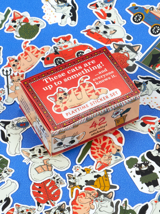 A box of These Cats Are Up To Something! Playtime Sticker Set containing 42 mini vinyl stickers featuring adorable cat faces, surrounded by individual cat stickers on a blue background.