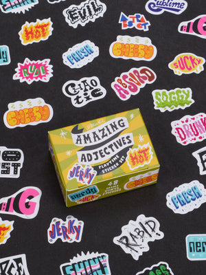 A yellow box labeled Amazing Adjectives Playtime Sticker Set from Blue Q is surrounded by a vibrant array of adjective stickers featuring descriptive words like jerky, hot, rude, soggy, and more—all designed to help modify nouns—set against a black background.