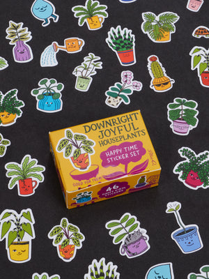 A yellow box labeled “Downright Joyful Houseplants Happy Time Sticker Set” by Blue Q sits surrounded by colorful, cartoon houseplant stickers with smiling faces on a black background—making it one of the most joyful gifts and perfect for adding fun to presents for teens or enhancing collectible figurine displays.