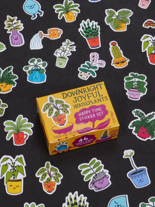 A yellow box labeled “Downright Joyful Houseplants Happy Time Sticker Set” by Blue Q sits surrounded by colorful, cartoon houseplant stickers with smiling faces on a black background—making it one of the most joyful gifts and perfect for adding fun to presents for teens or enhancing collectible figurine displays.