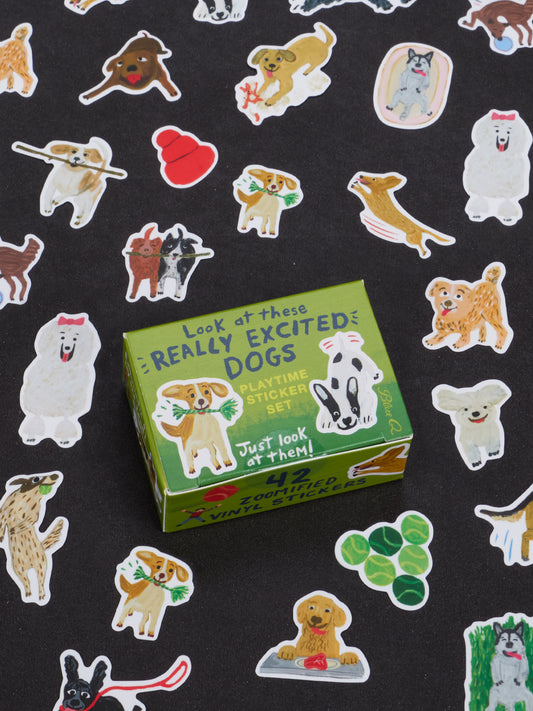 A box labeled “Look At These Really Excited Dogs Playtime Sticker Set” by Blue Q is surrounded by an array of colorful dog stickers on a black background. Reminiscent of a cute collectible figurine collection, the stickers feature dogs in playful poses along with other dog-related items.