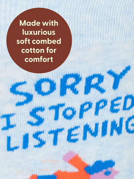 Close-up of Blue Q Sorry I Stopped Listening M-Crew Socks, made from soft combed cotton for comfort. Features blue text and a small cartoon figure. Fits men's shoe size 7-12.