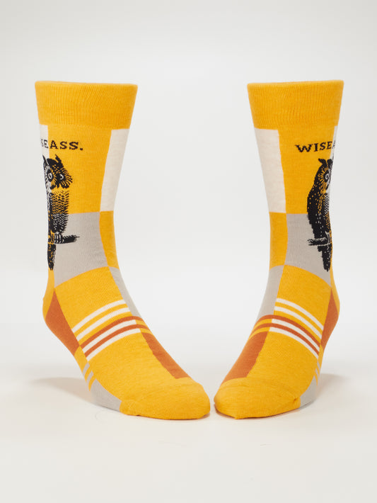 Blue Q Wiseass M-Crew Socks are yellow men's socks with an owl illustration, "WISEASS" text, white, orange, and gray geometric patterns and toe stripes, made from soft combed cotton for comfort.