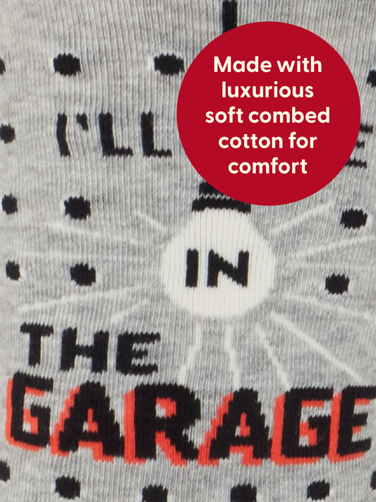 Close-up of the Blue Q I’ll Be In The Garage M-Crew Socks, featuring the phrase “ILL BE IN THE GARAGE” knit into soft gray fabric with black and red accents. Made from luxurious combed cotton for maximum comfort—perfect for puttering or tinkering in the garage. A red circle highlights this cozy detail on the socks.