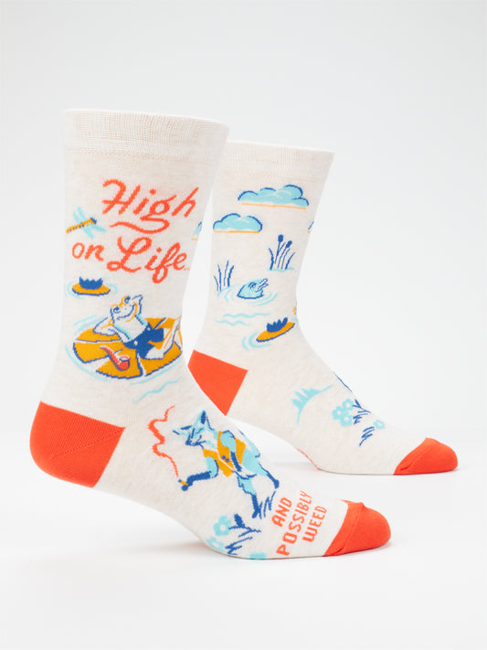 Blue Q High On Life...And Possibly Weed M-Crew Socks are crafted from cream combed cotton and feature orange toes and heels. Designed to fit men's shoe sizes 7–12, these socks showcase a cartoon animal relaxing in an inner tube surrounded by playful water and cloud motifs, along with the whimsical text: "High on Life—and possibly weed.