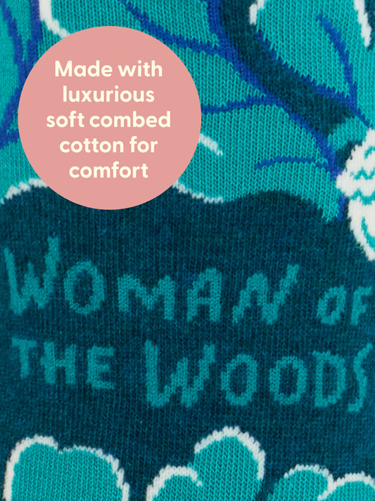 Close-up of Blue Q's Woman Of The Woods W-Crew Socks in teal and blue, featuring "WOMAN OF THE WOODS" text, a foraged berry pattern, and a pink circle overlay: Made with luxurious soft combed cotton for comfort.