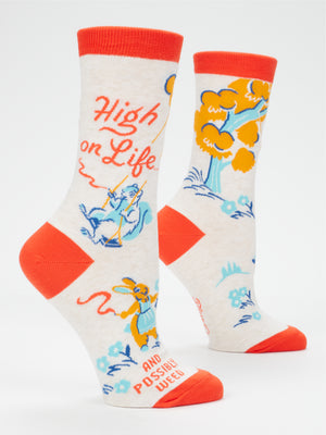 Step into style and humor with the Blue Q High On Life...And Possibly Weed W-Crew Socks—a vibrant pair of combed cotton socks with red heels and cuffs, showcasing a playful blue squirrel, orange trees, and the phrase "High on Life" and "And Possibly Weed" against a light background. Designed to fit women's shoe size 5–10.