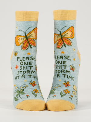 Blue Q’s “Please, One Shitstorm At A Time” W-Ankle Socks are blue combed cotton with yellow toes, heels, cuffs, an orange butterfly, flowers, and the phrase printed on the front.