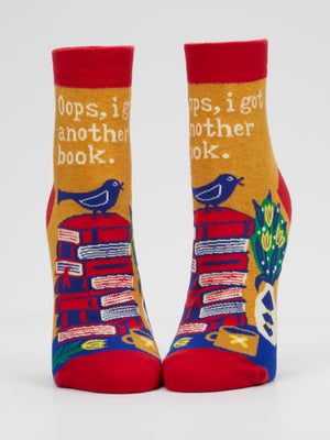 Add a literary touch to your wardrobe with Blue Q’s “Oops, I Got Another Book. W-Ankle Socks.” These vibrant women’s ankle socks feature whimsical stacks of books, cheerful birds, and a plant alongside the playful phrase “Oops, I got another book.” Primarily in red, yellow, and blue hues, they’re the perfect gift for any reading enthusiast.