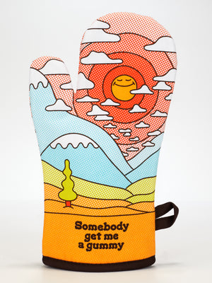 The Blue Q Somebody Get Me A Gummy Oven Mitt is super-insulated and colorful, with a cartoon landscape—hills, tree, smiling sun—and "Somebody get me a gummy" printed at the bottom. Perfect for any kitchen!.