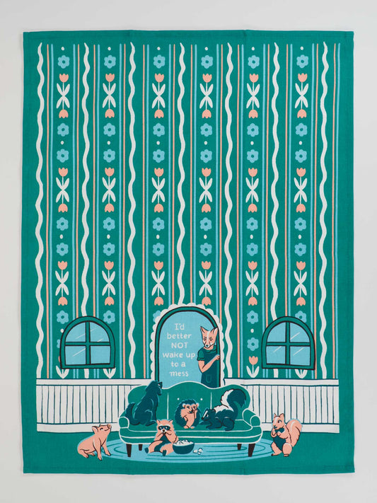 The Blue Q "I'd Better Not Wake Up To A Mess" Dish Towel is super-absorbent, with teal and peach colors, featuring playful cats on a green couch in a striped, floral wallpapered room.