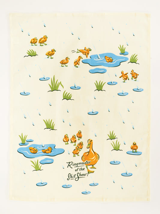 The Blue Q Ringmaster Of The Shitshow Dish Towel is a super-absorbent, unbleached cotton kitchen towel with ducks and ducklings in rainy grass and puddles, adding humor to your dish towel collection.