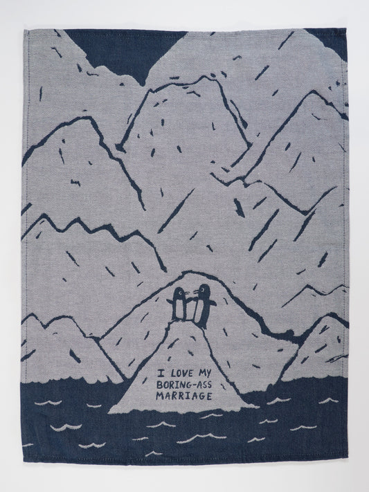 The Blue Q "I Love My Boring-Ass Marriage" Dish Towel features a mountain and water scene with two figures on a hill above the phrase "I LOVE MY BORING-ASS MARRIAGE," all in dark blue lines on gray.