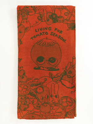 The Living For Tomato Season Dish Towel by Blue Q is a red unbleached cotton towel with a smiling cartoon tomato, the phrase “LIVING FOR TOMATO SEASON,” and doodled veggies like carrots, radishes, and sliced tomatoes.