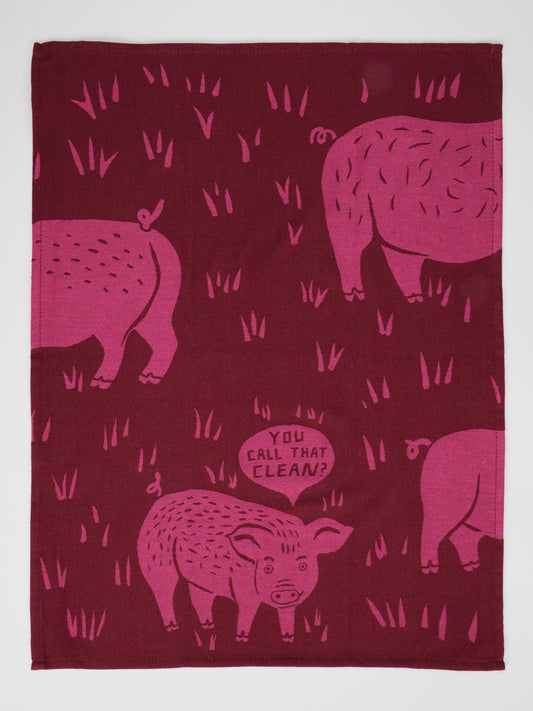 The Blue Q “You Call That Clean? Dish Towel” features playful pink pig and grass illustrations on maroon unbleached cotton, with one pig humorously asking, “You call that clean?” in a speech bubble. This super-absorbent towel adds a fun touch to any kitchen.